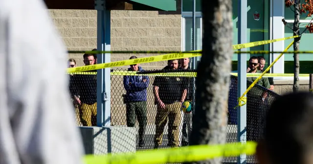Police officers are seen behind a fence and yellow crime scene tape at an outdoor location.