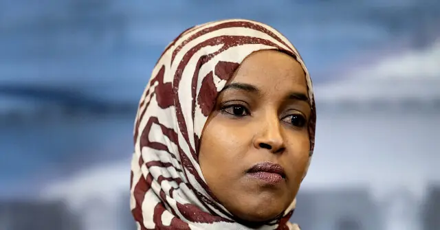 The image shows a person wearing a patterned hijab, with a blurred background that appears to be an outdoor setting.