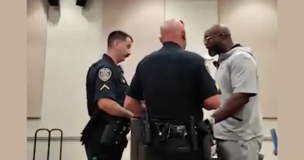 A man is being escorted by two police officers in a courtroom setting.