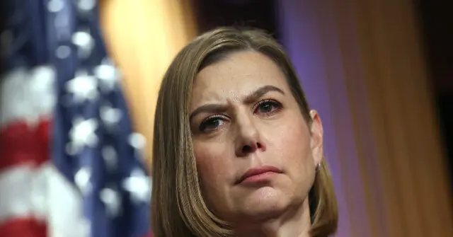 The image shows a person with a serious expression, set against a backdrop featuring an American flag.