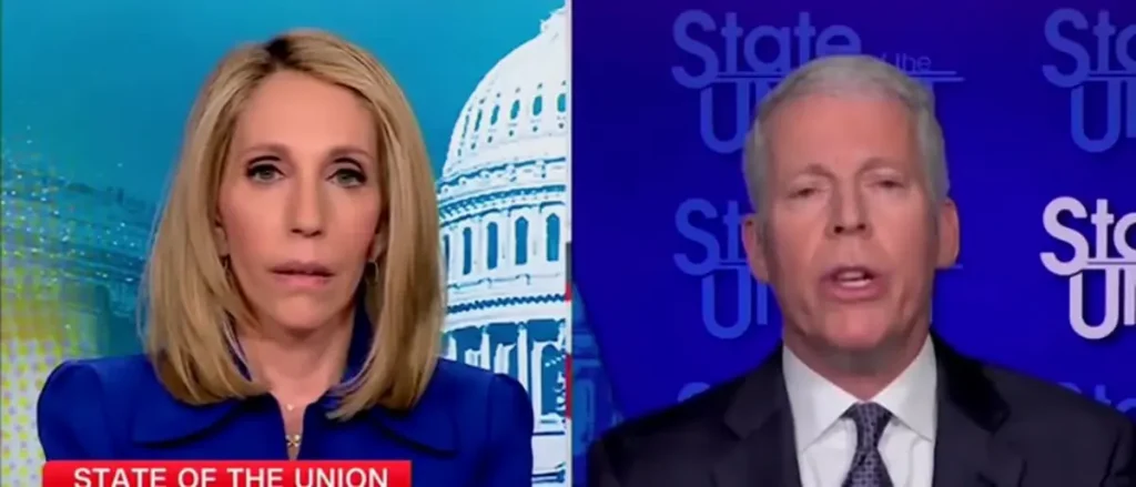 The image shows two individuals participating in a "State of the Union" broadcast, with one person on the left wearing a blue outfit and the other on the right in a suit, set against a backdrop featuring the Capitol building.