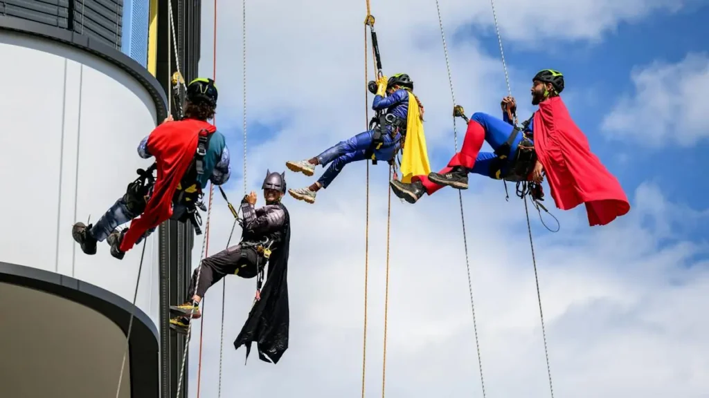 A group of people dressed as superheroes rappel down the side of a tall building.