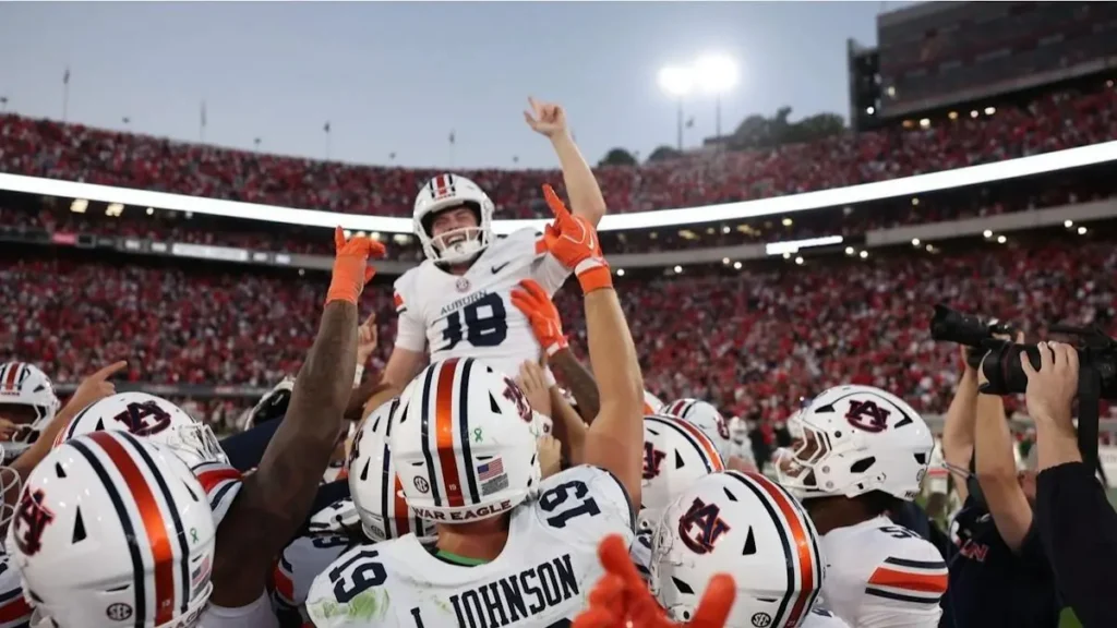 Auburn football players celebrate a victory with their teammates in a stadium filled with fans.