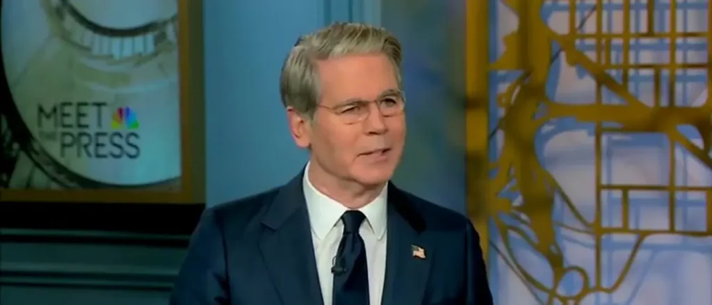 The image shows a man in a suit and tie on a television show set, with the "Meet the Press" logo visible in the background.