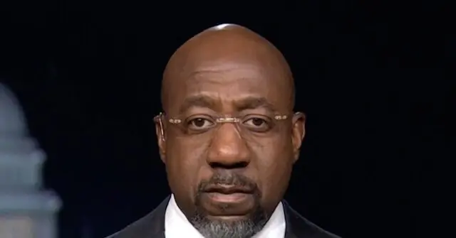 The image shows a man wearing glasses and a suit, appearing to be in a formal or professional setting.