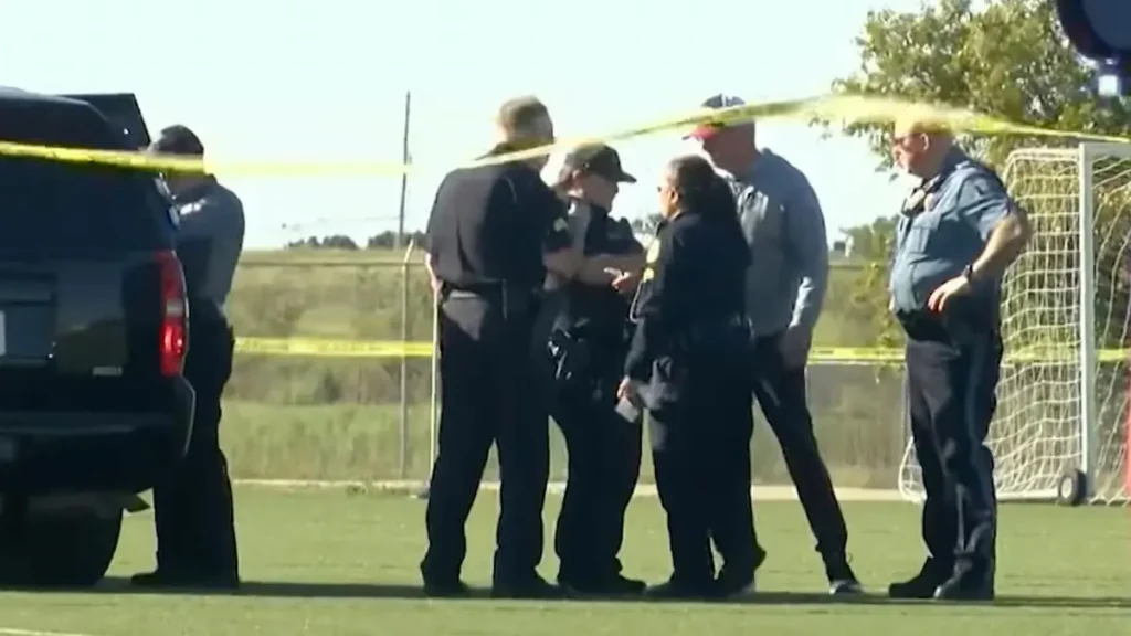 Police officers are gathered at a crime scene marked by yellow tape on a soccer field.