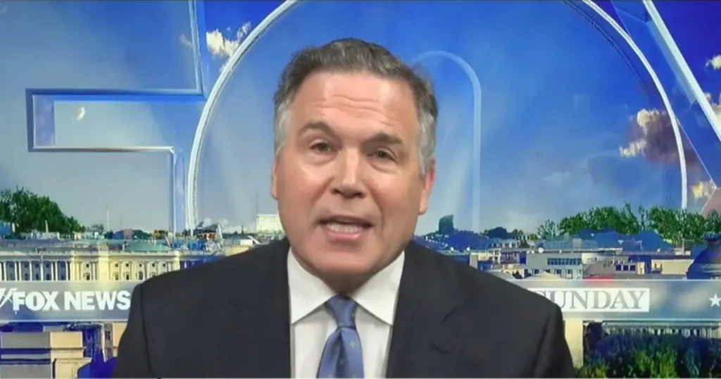 The image shows a news anchor on a Fox News broadcast, with a cityscape and sky backdrop.