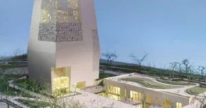 The image depicts a modern architectural design featuring a tall, intricate tower and a lower building with curved edges, surrounded by a landscaped area with trees.