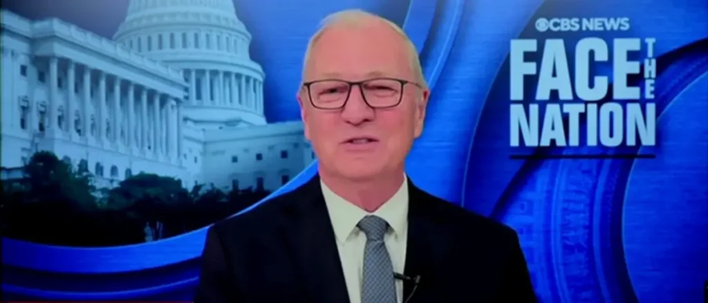 The image shows a news anchor on the set of CBS News' "Face the Nation," with the Capitol building in the background.