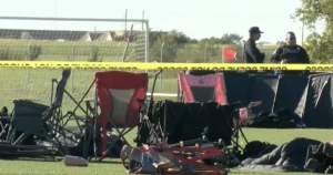 The image shows a crime scene with police tape, camping chairs, and a red flag, indicating an investigation in progress.