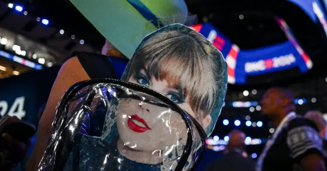 A person is holding a large, wrapped object in a stadium setting with bright lights and a scoreboard in the background.