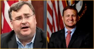 The image shows two men in suits, one speaking and the other smiling, with American flags in the background, suggesting a political or governmental setting.