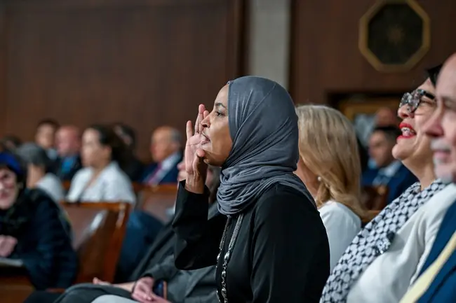 A woman in a hijab is seen clapping during a formal event in a courtroom setting.