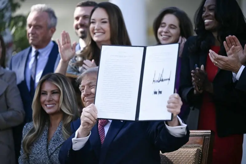 The image shows a person holding up a signed document in front of a group of people who are clapping and smiling.