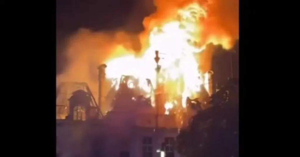 A building is engulfed in flames, with intense fire and smoke billowing into the night sky.