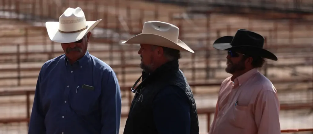 Three men wearing cowboy hats are standing together in what appears to be an outdoor arena or event setting.