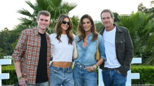 The photo shows four individuals posing together outdoors, with palm trees and greenery in the background.