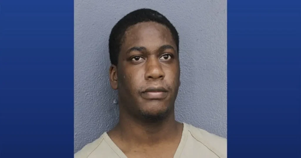 The image is a mugshot of a man in a light-colored shirt against a plain background.