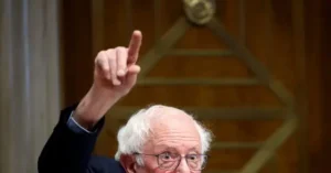 The image shows a person raising their index finger, possibly emphasizing a point during a speech or presentation.