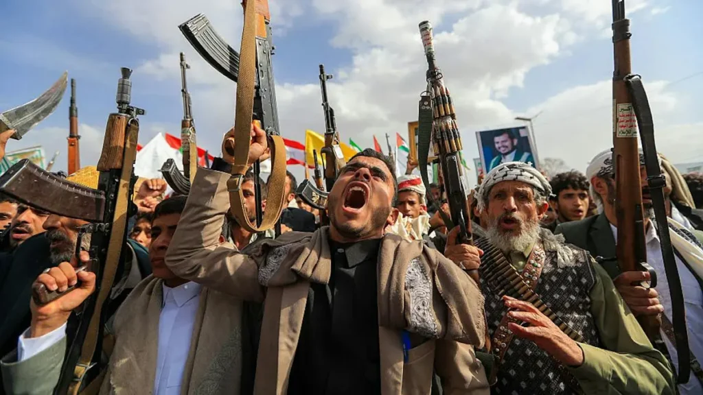 A group of individuals holds up weapons and appears to be shouting or chanting in a public gathering.