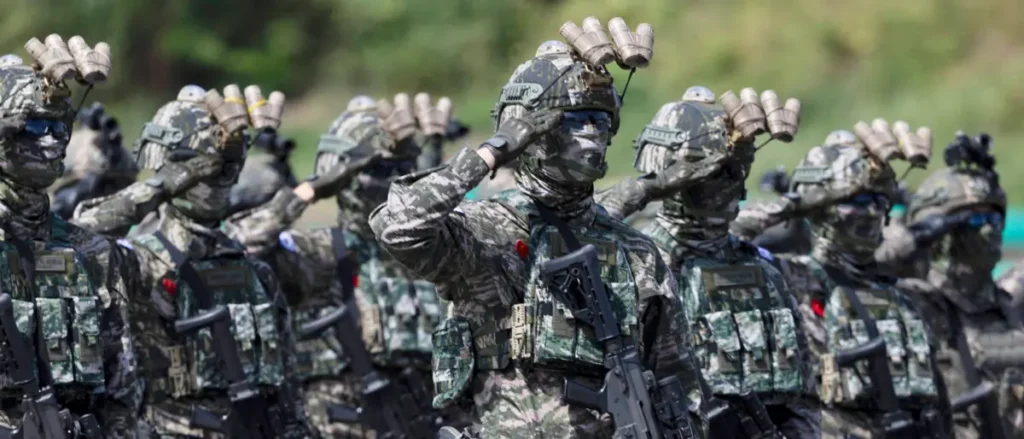 A group of soldiers in camouflage uniforms and tactical gear are saluting in formation.