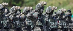 A group of soldiers in camouflage uniforms and tactical gear are saluting in formation.