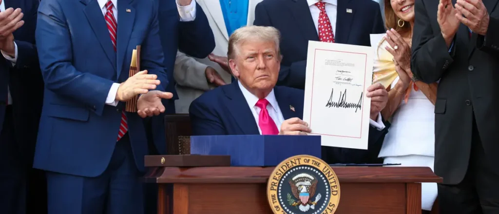 The image shows a formal event where a person is holding a document and standing at a podium with the seal of the President of the United States, while others clap and observe.