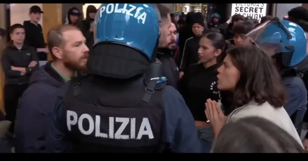 A police officer in a "Polizia" uniform is engaged in a conversation with a man and a woman in a crowded urban setting.
