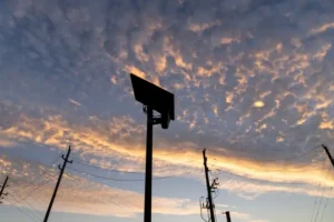 The image captures a silhouette of a basketball hoop against a vibrant sunset sky, with power lines and poles in the foreground.