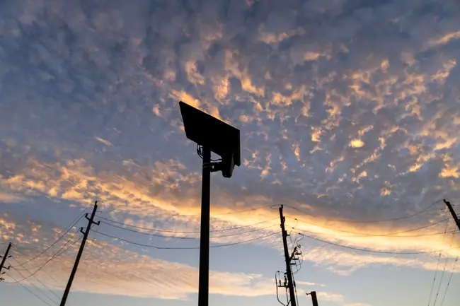 The image captures a silhouette of a basketball hoop against a vibrant sunset sky, with power lines and poles in the foreground.