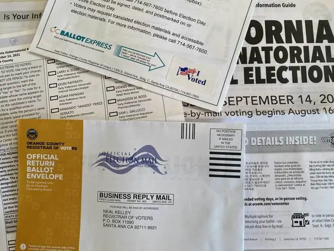 The image shows various election-related materials, including a ballot envelope, a voter information guide, and a "I Voted" sticker, indicating preparations for a California gubernatorial election.