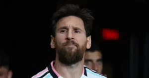 The image shows a close-up of a person wearing a striped jersey, with a dark background and a red exit sign visible in the distance.