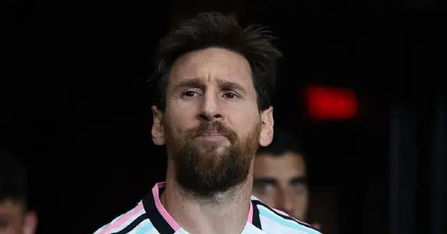 The image shows a close-up of a person wearing a striped jersey, with a dark background and a red exit sign visible in the distance.