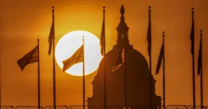 The sun sets behind a historic building adorned with flags, creating a dramatic silhouette.