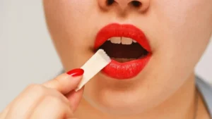 A person with red lipstick is holding a white object near their mouth.
