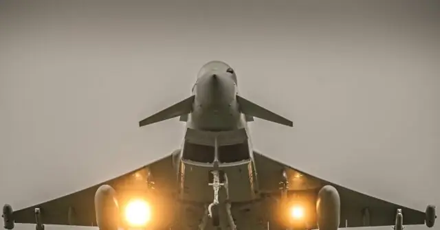 A fighter jet is captured from a low angle, with its engines glowing brightly against a hazy sky.