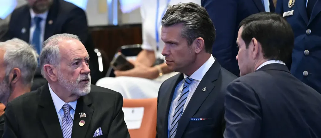 The photo shows a group of men in formal attire engaged in conversation at what appears to be a formal event or meeting.