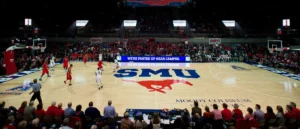 A basketball game is being played at SMU's Moody Coliseum, with a large crowd in attendance.