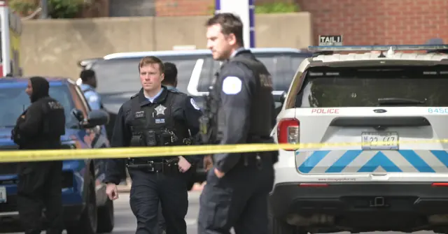 Police officers are seen at a crime scene with a yellow tape barrier and a police vehicle in the background.