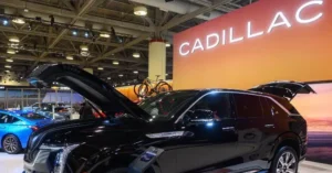 A Cadillac vehicle is displayed at an auto show with its hood and trunk open, showcasing its features.