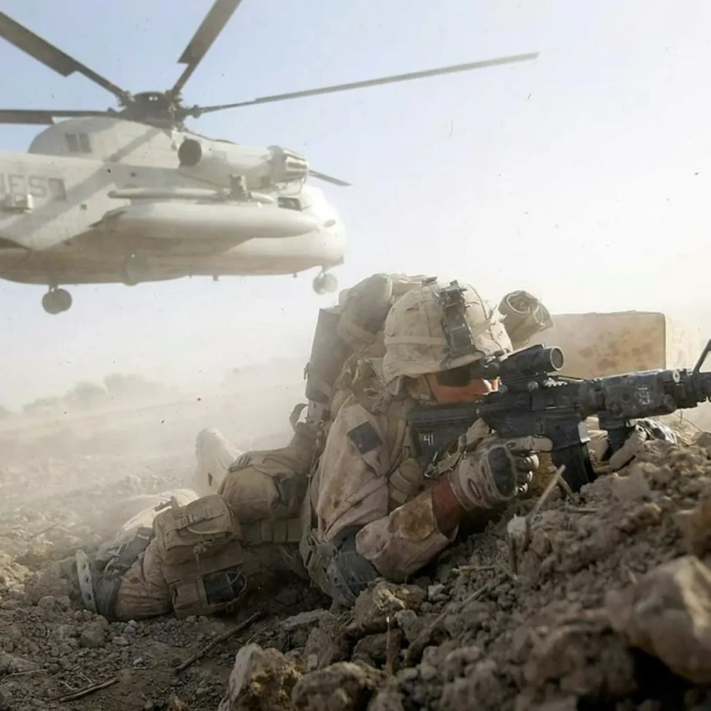 A soldier takes cover while a helicopter hovers in the background during a military operation.