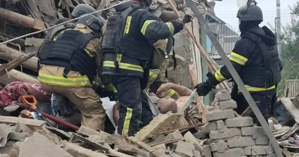 Rescue workers are seen searching through the rubble of a collapsed building, indicating a disaster response operation.