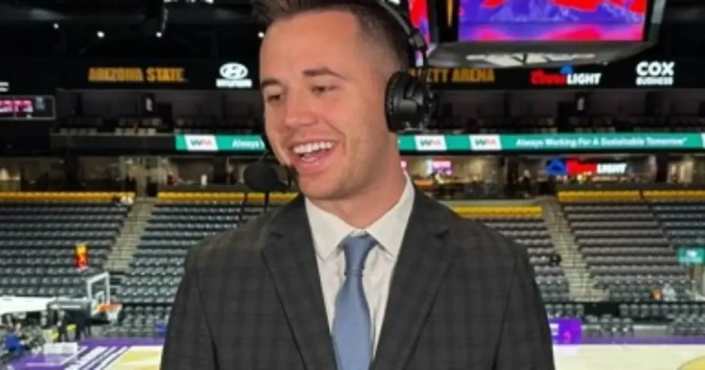 A man in a suit and tie is smiling in front of an empty basketball arena.