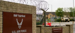 The image shows the entrance to RAF Fairford, a U.S. Air Force base, with a sign indicating the command chief's name and a military vehicle visible in the background.
