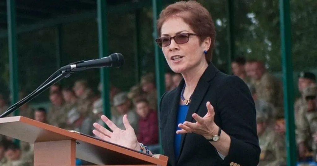A woman is giving a speech at a podium in front of a group of people, likely at a formal or military event.