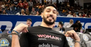 A person is holding up a shirt that defines "woman" as "adult human" in a humorous or satirical context at a basketball game.