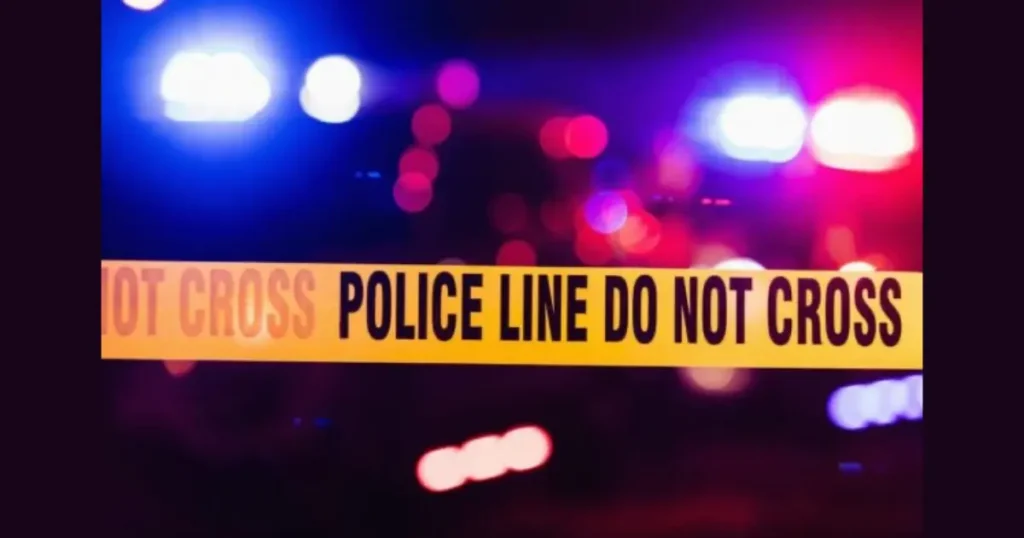 The image shows a "POLICE LINE DO NOT CROSS" tape with blurred police lights in the background, indicating a crime scene or police activity.