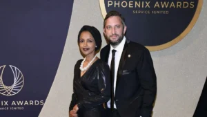 Two individuals pose together at the Phoenix Awards event, showcasing formal attire and a backdrop featuring the event's logo.