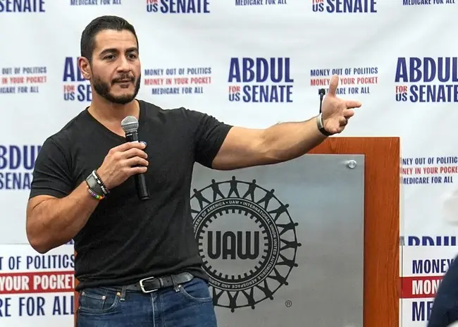 A man speaks at a podium with a UAW logo, addressing an audience at a campaign event for Abdul for US Senate.