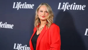 A woman in a red blazer poses in front of a backdrop featuring the "Lifetime" logo.